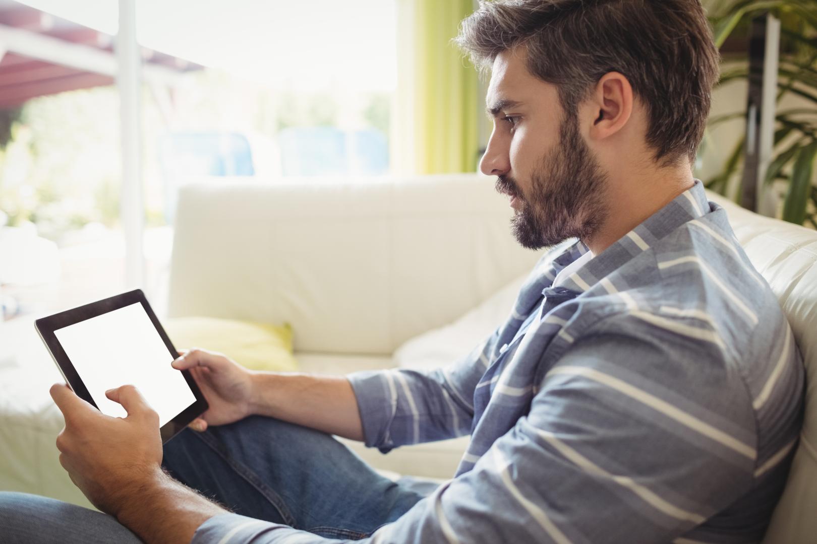 Man using digital tablet while relaxing on sofa stock photo