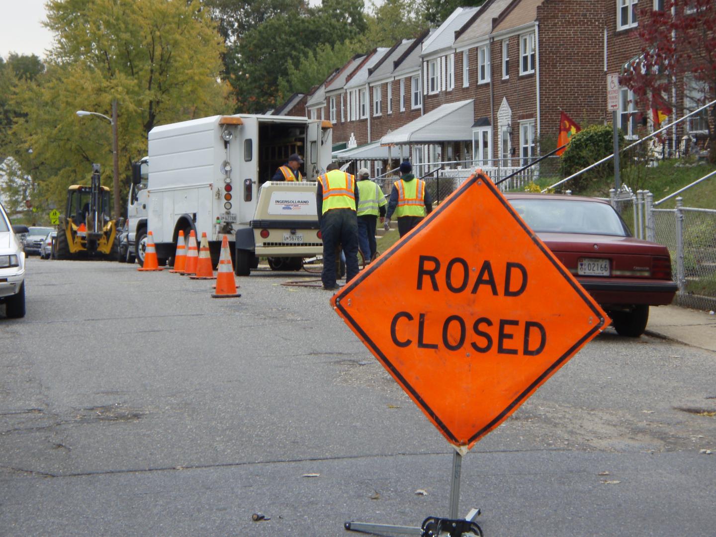 An image of a street with an orange diamond shaped "Road Closed" sign