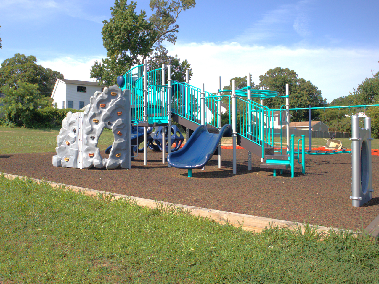 Colorful outdoor playground with mulch on the ground. Bright blue skies and green grass.