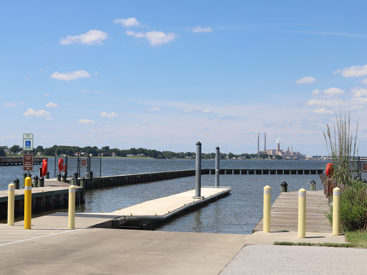 Boat ramp and wooden floating dock extending into calm blue water under a clear sky at Fort Smallwood Park.