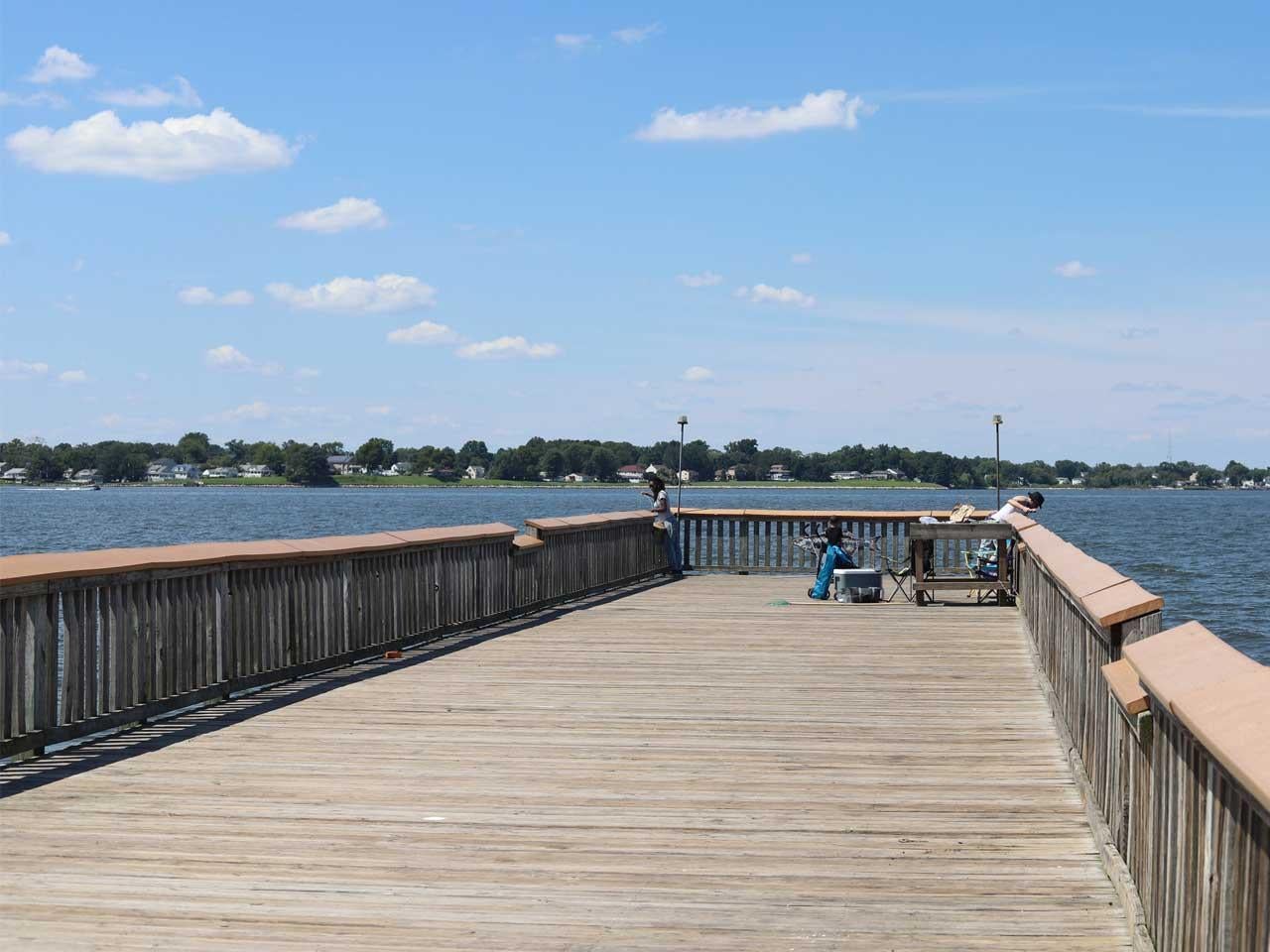 Long fishing pier with a couple people fishing with bright blue skies and a few clouds.
