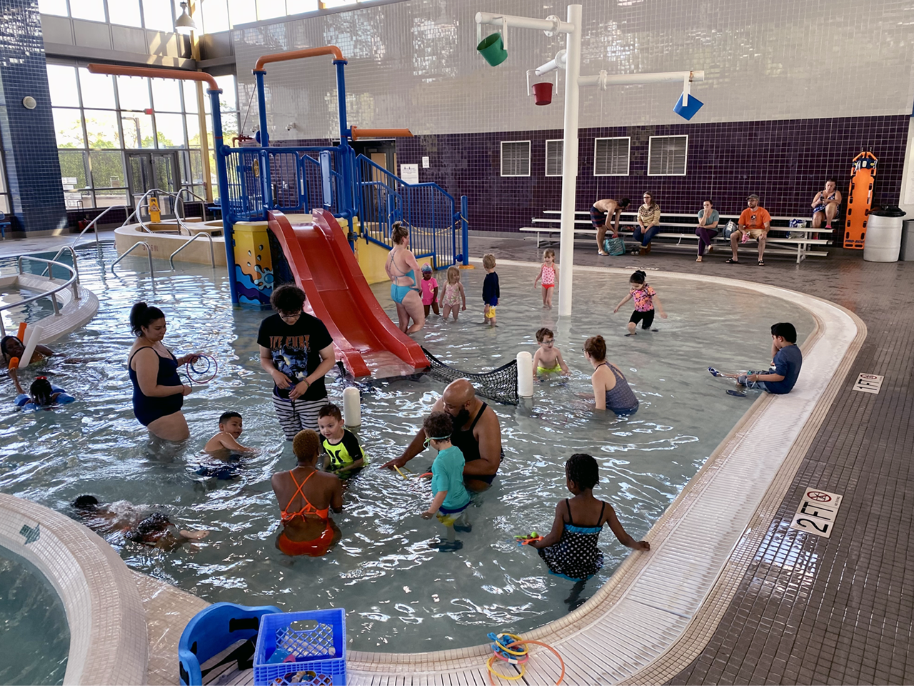 Indoor swimming pool with many children and adults playing in the water park pool.